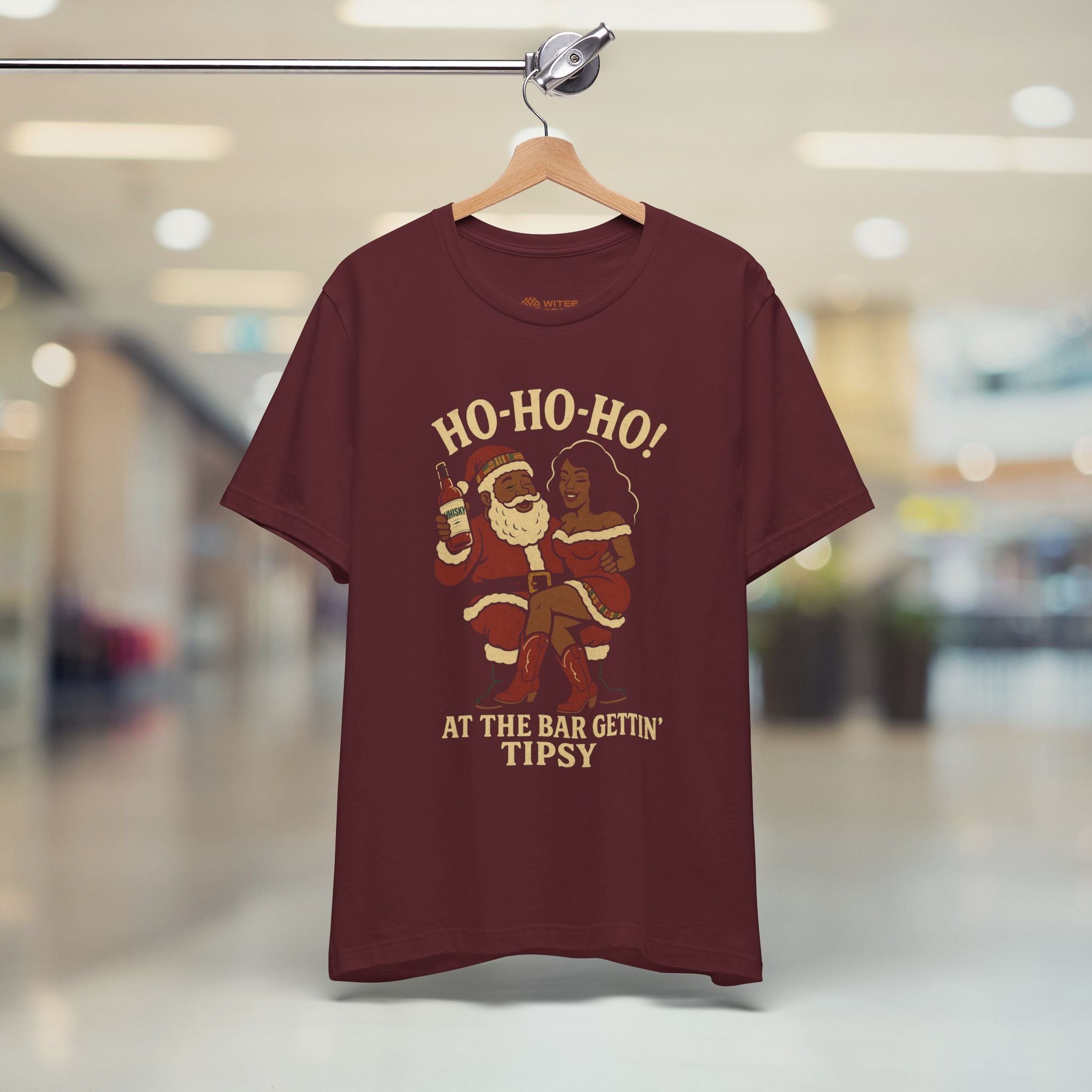 Maroon t-shirt with Christmas-themed design on a hanger in a store.