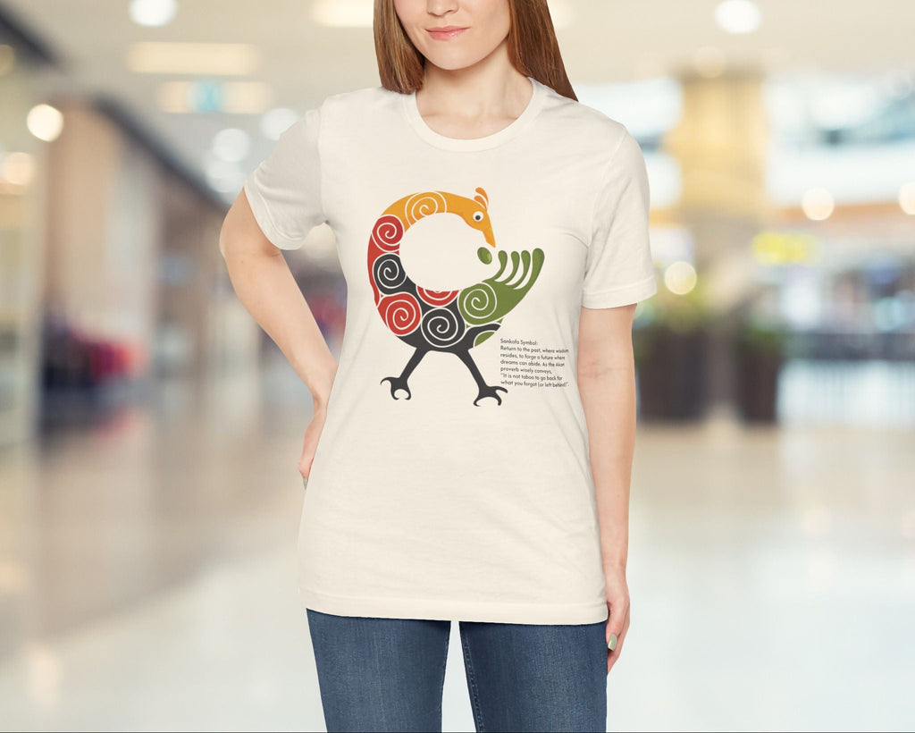 Woman wearing a beige t-shirt with a colourful bird design in a blurred indoor setting