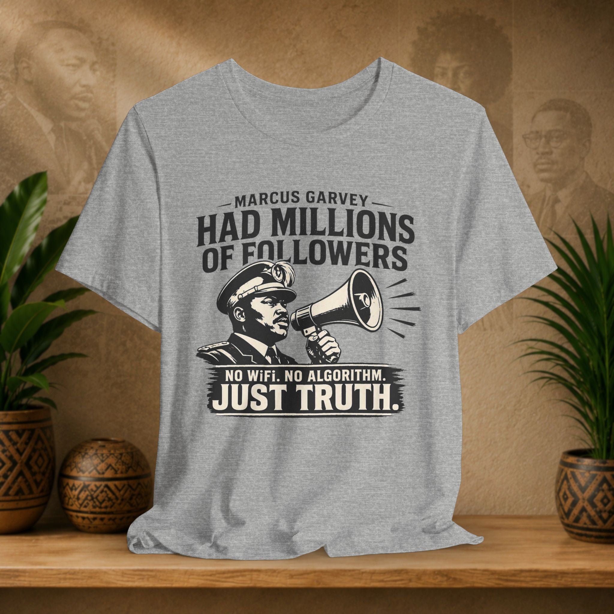 Gray t-shirt with a graphic and text on a wooden surface with plants and a textured wall background