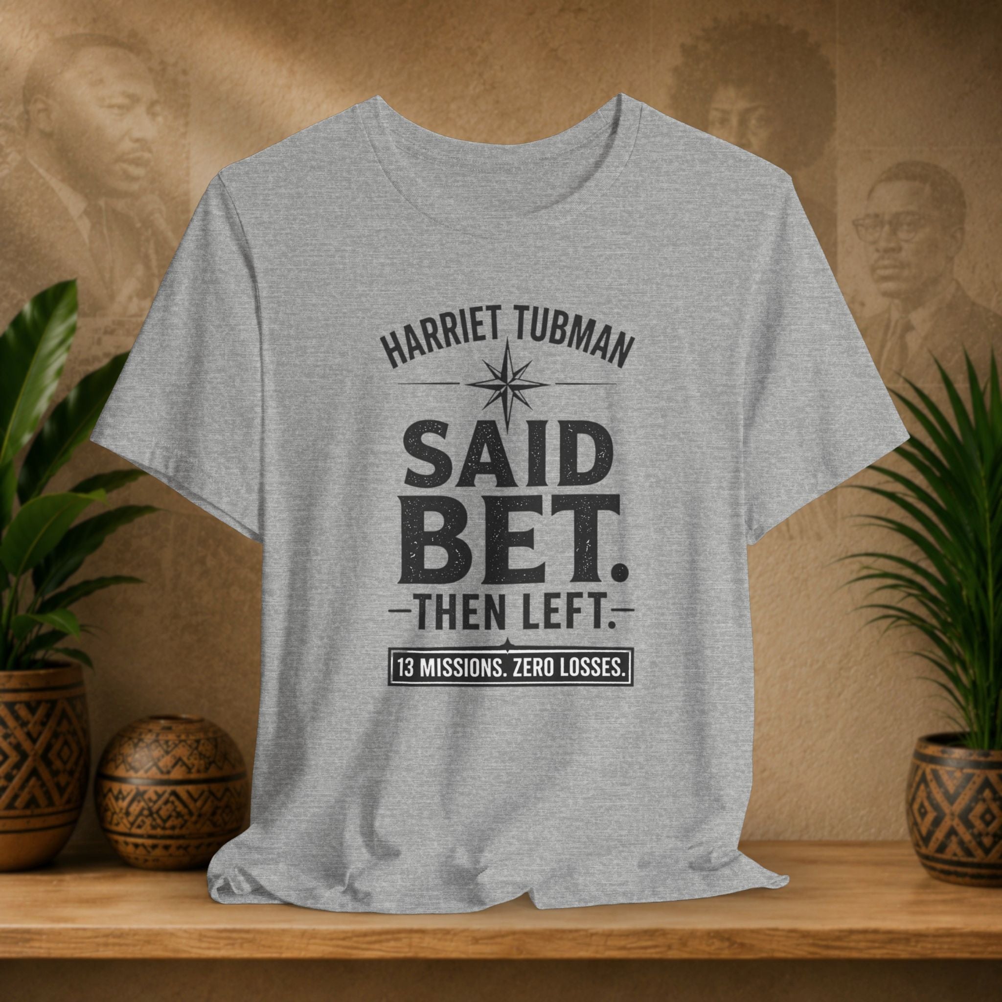 Gray t-shirt with text on a wooden shelf with plants and decorative items.