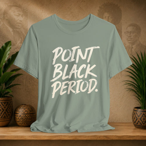 A sage green crewneck t-shirt with the text 'POINT BLACK PERIOD.' printed in a white brush-stroke font, displayed on a wooden shelf with potted plants and a textured background.