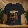 Black t-shirt with 'Soft Life. Hard History. Balanced Vibes.' text on a wooden surface with plants and decorative items.
