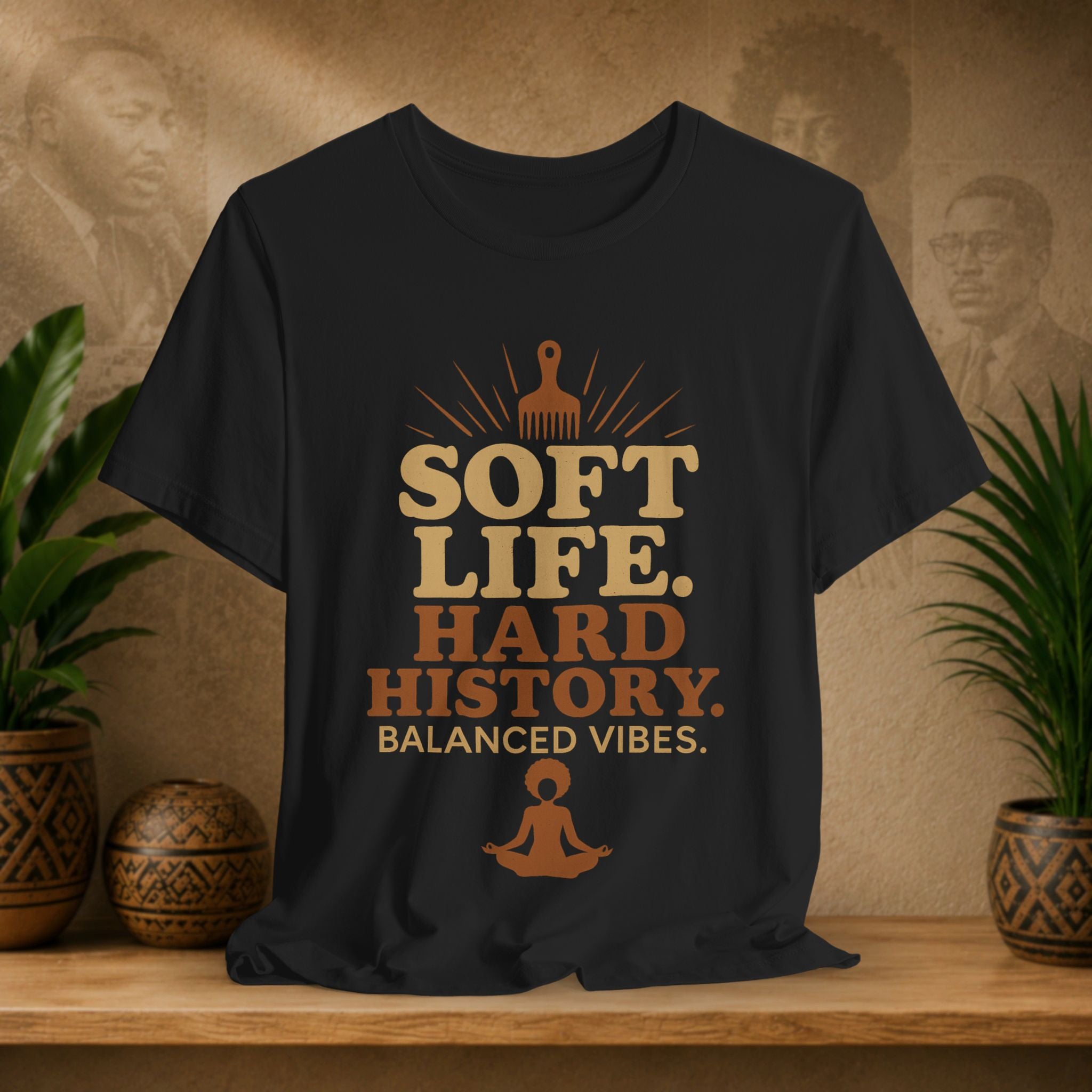 Black t-shirt with 'Soft Life. Hard History. Balanced Vibes.' text on a wooden surface with plants and decorative items.