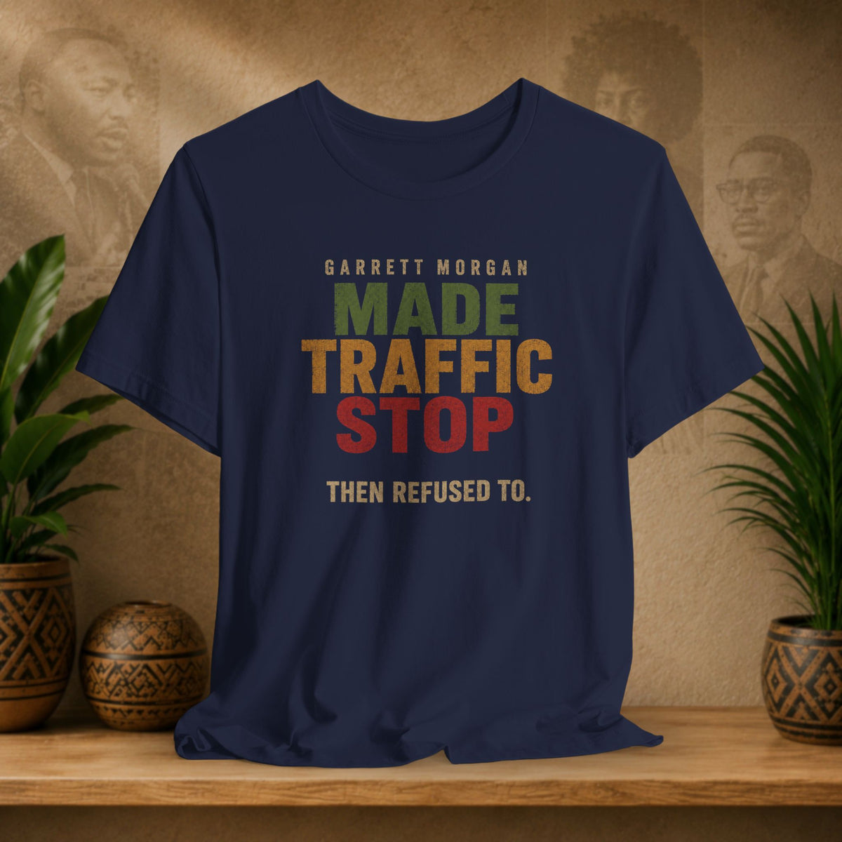 A navy blue graphic t-shirt displayed on a wooden shelf. The shirt features a retro-style text graphic that reads 'GARRETT MORGAN MADE TRAFFIC STOP THEN REFUSED TO.