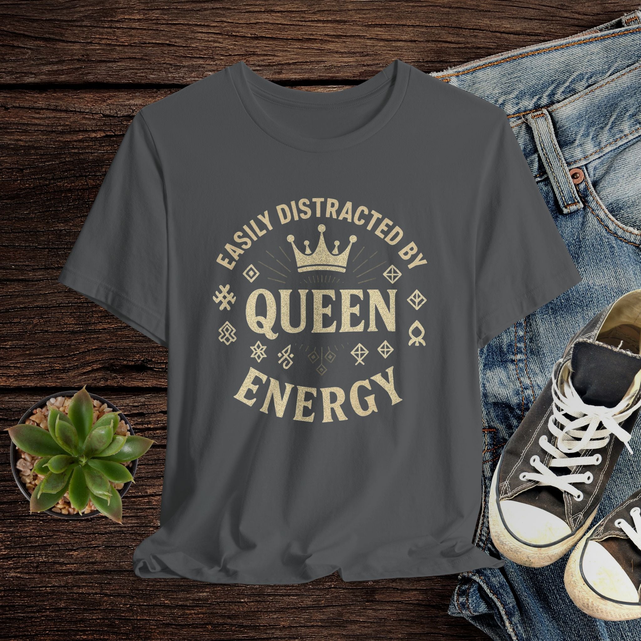 Gray t-shirt with 'Easily Distracted by Queen Energy' text on a wooden surface with jeans and sneakers.