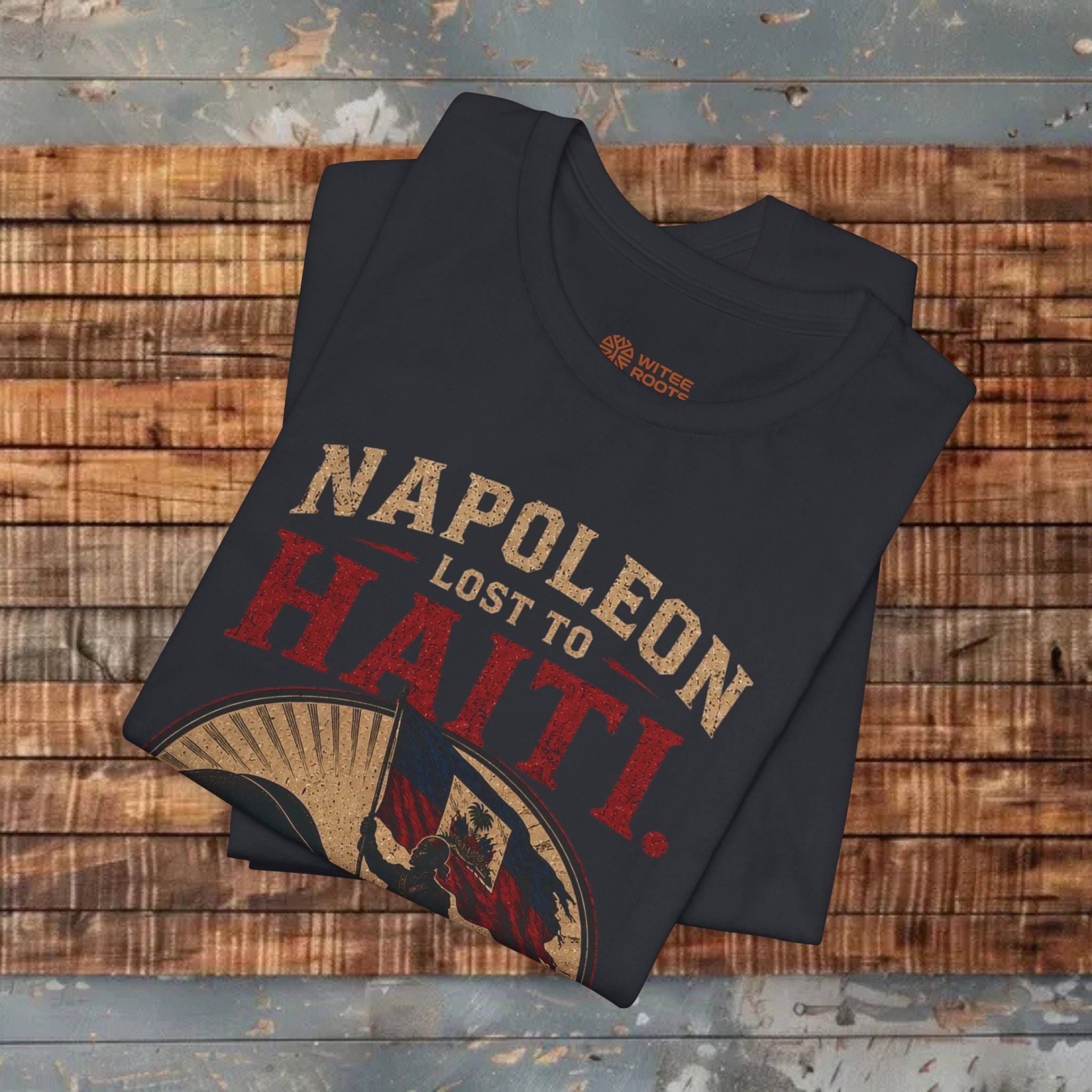 Folded black t-shirt with 'Napoleon Lost to Haiti' design on a wooden surface