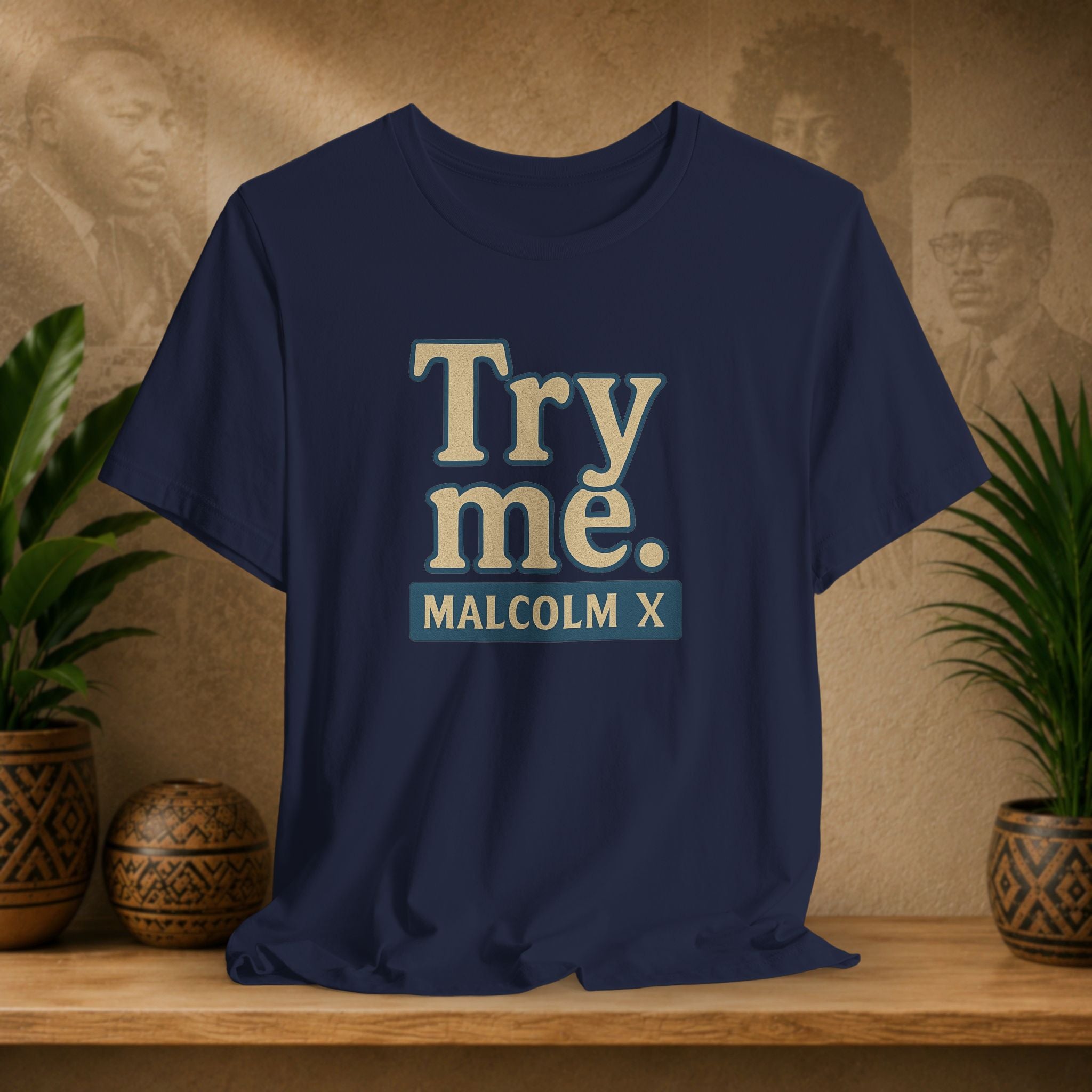 Navy blue t-shirt with 'Try me. MALCOLM X' text on a wooden surface with plants and a textured wall background.