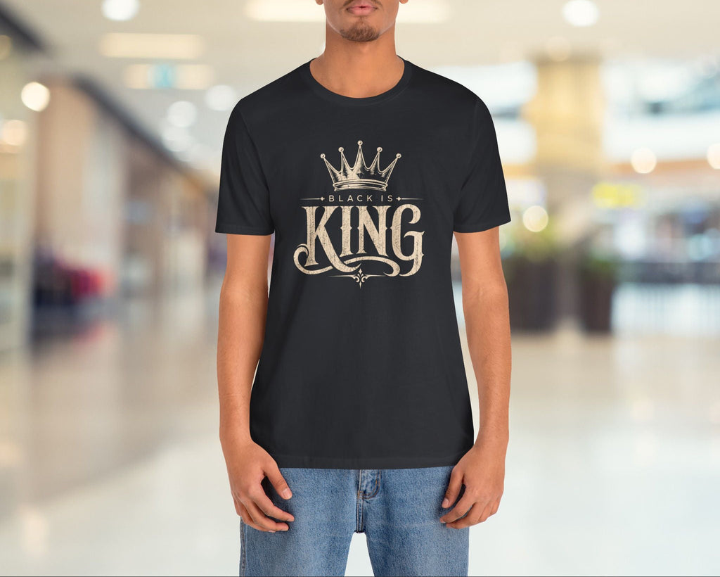 Person wearing a black t-shirt with 'Black is King' design in a blurred indoor setting