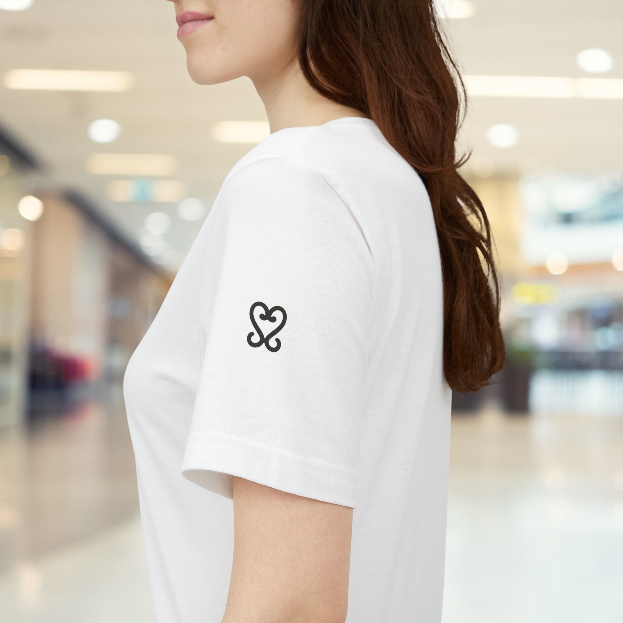 Person wearing a white t-shirt with a black heart design in a blurred indoor setting