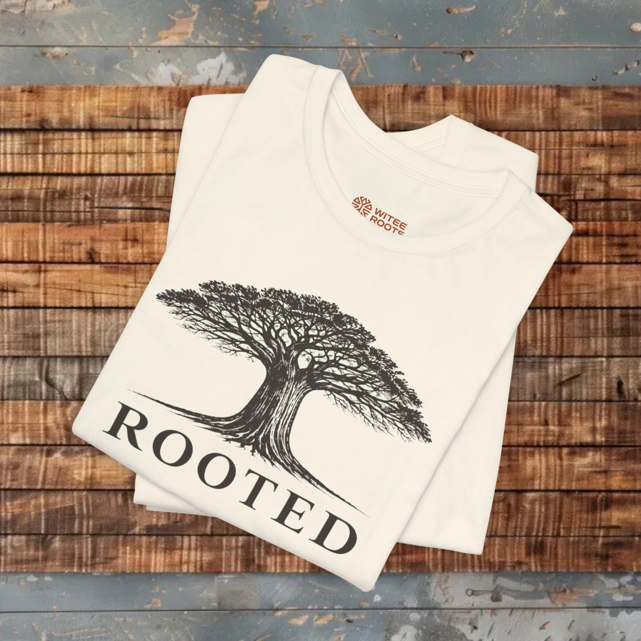Beige t-shirt with tree design and 'Rooted' text on a wooden surface