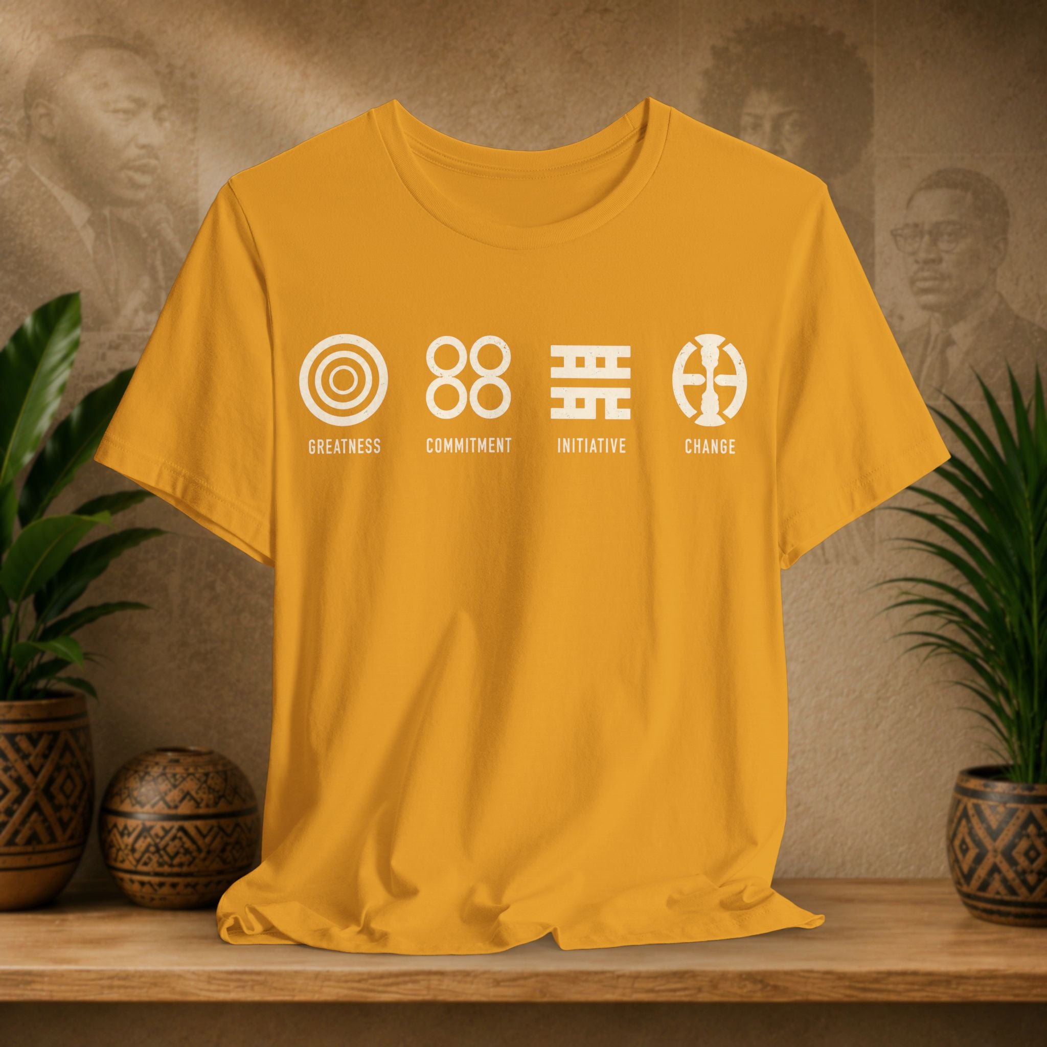 Yellow t-shirt with white graphics and text on a wooden surface with plants and a textured wall background