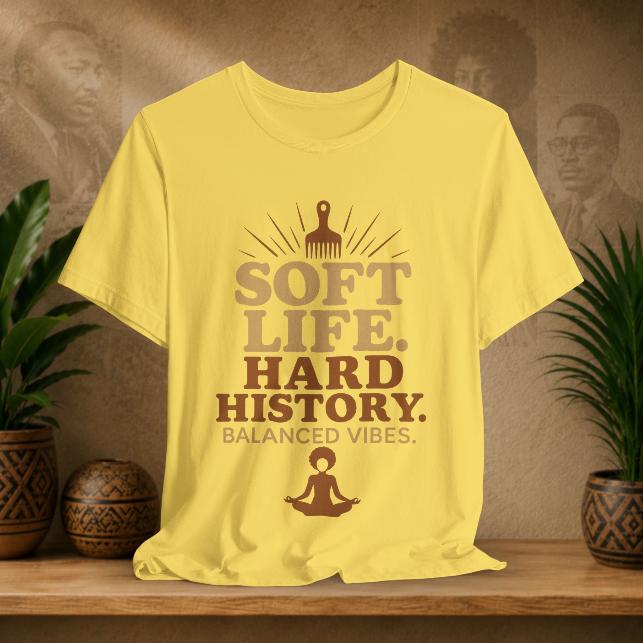 Yellow t-shirt with text and graphics on a wooden surface with plants and a textured wall background