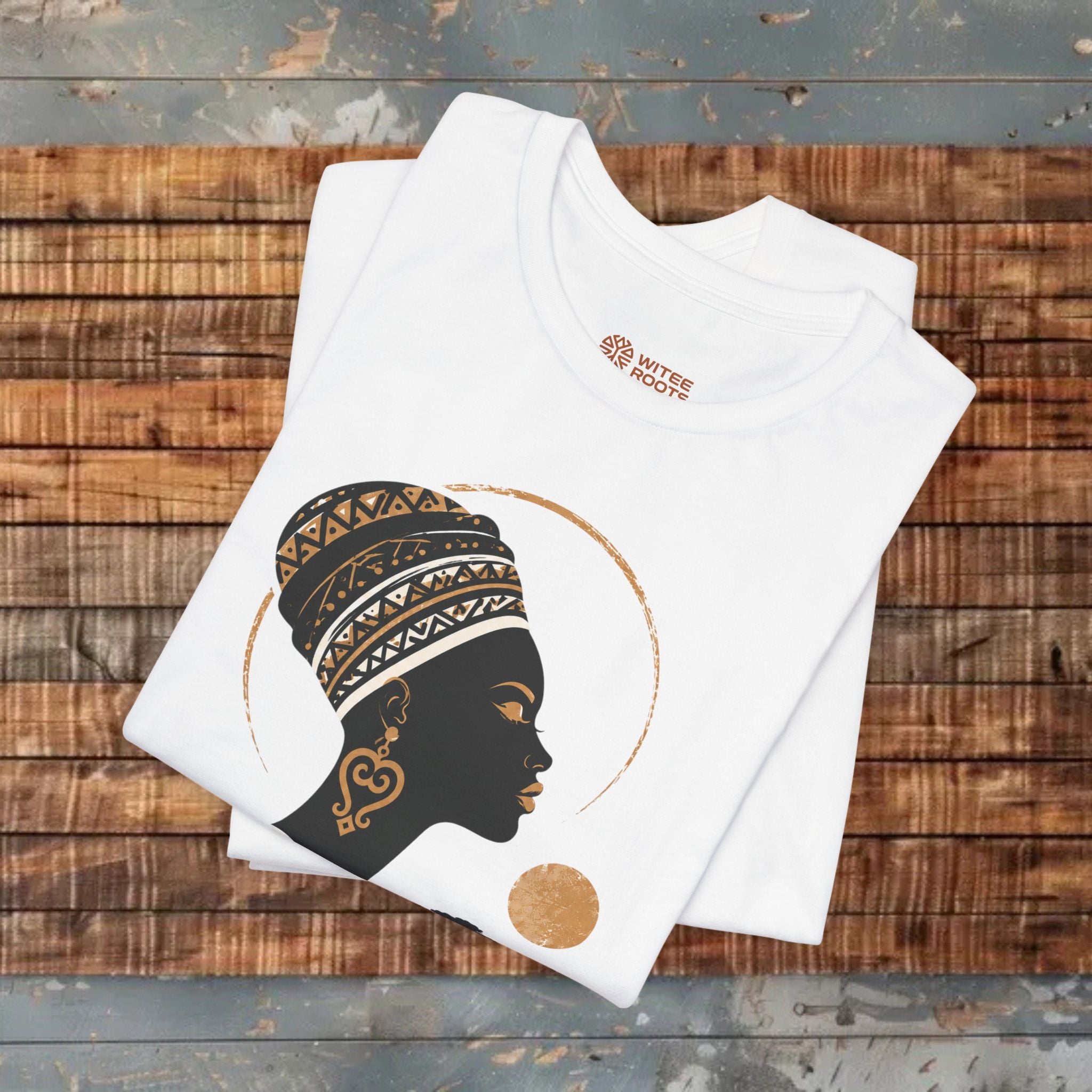 White t-shirt with a black and gold graphic of a woman's headscarf on a wooden surface