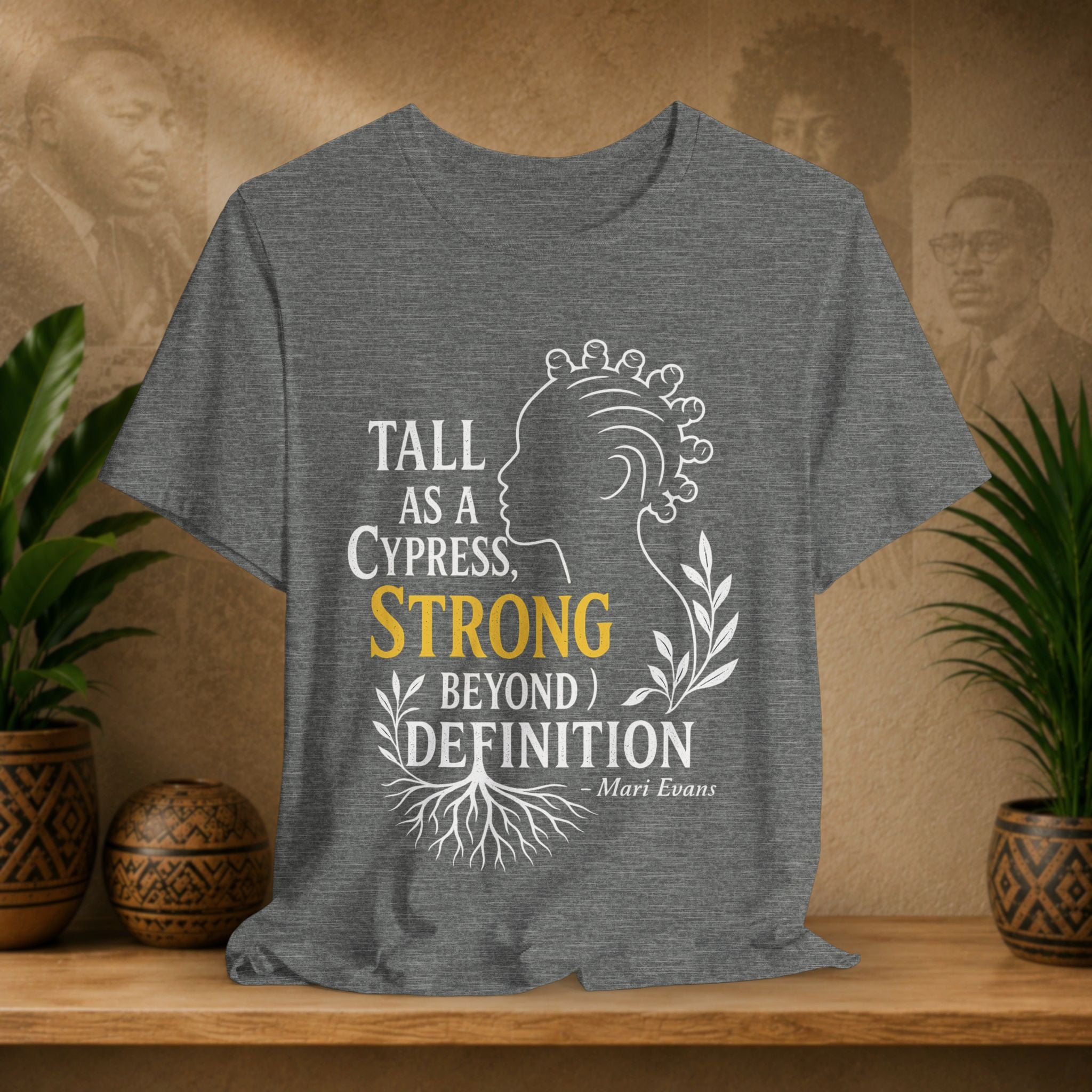 Gray t-shirt with a design and text on a wooden surface with plants and a decorative item in the background.