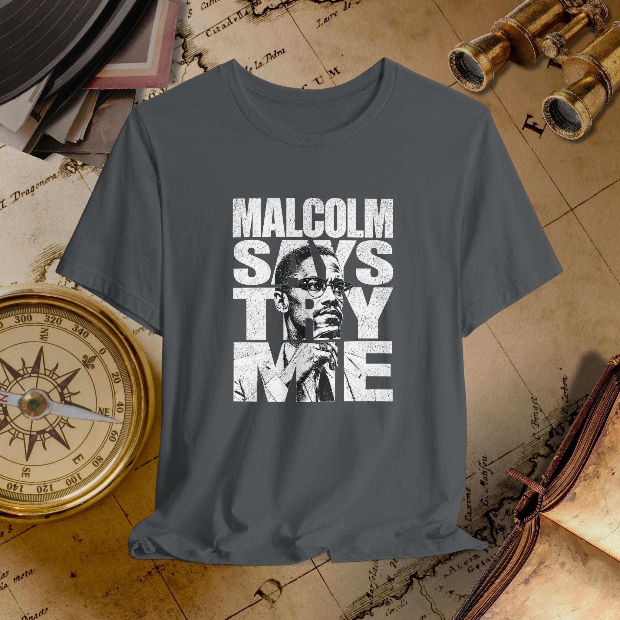 Gray t-shirt with 'Malcolm Says Thy Name' graphic on a vintage map background