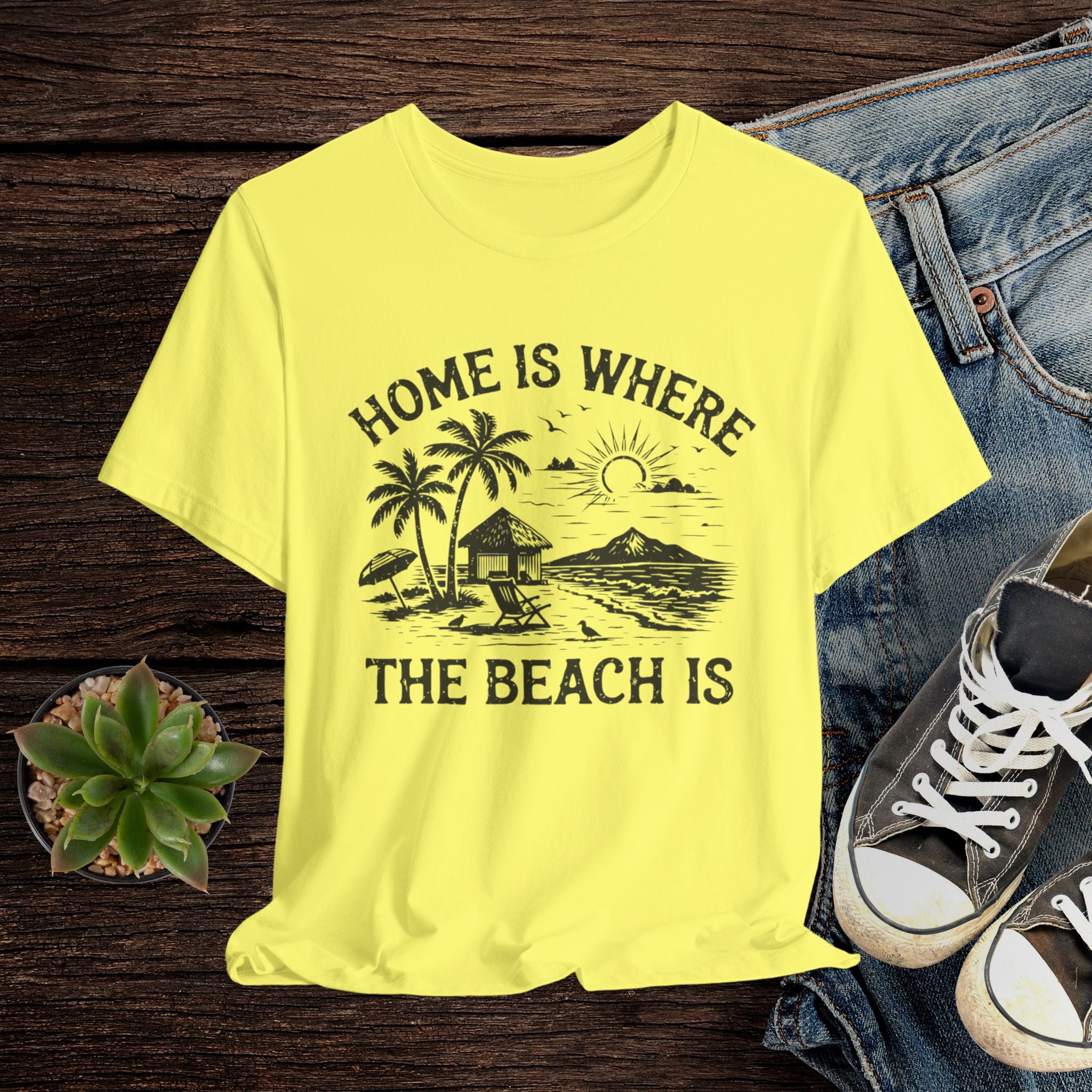 Yellow t-shirt with beach graphic and text on a wooden surface with jeans and sneakers.
