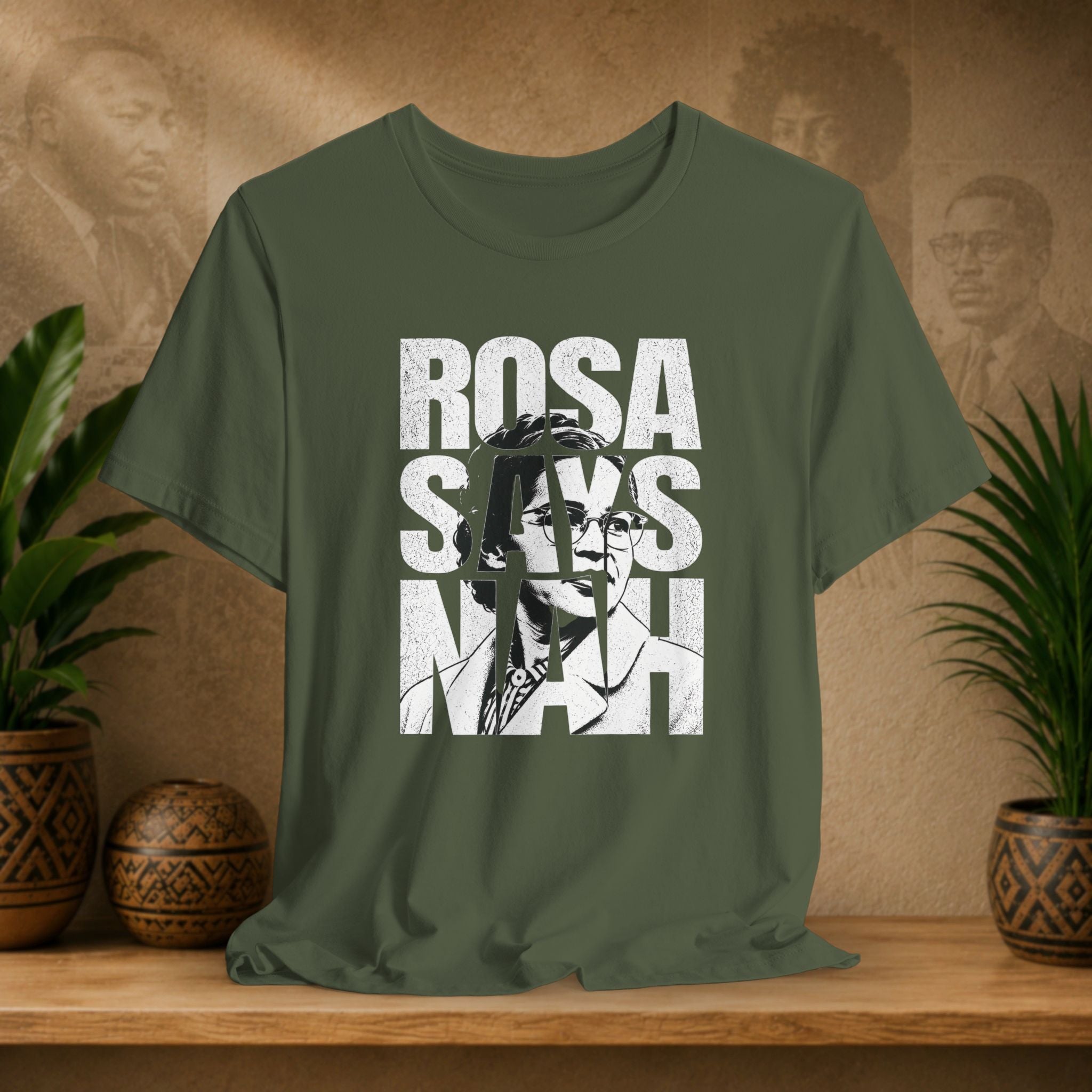 Green t-shirt with 'Rosa Parks' graphic design on a wooden surface with plants and a textured wall in the background.