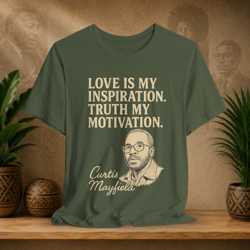 Green t-shirt with text and a portrait of Curtis Mayfield on a wooden surface with plants and a wall with portraits in the background.