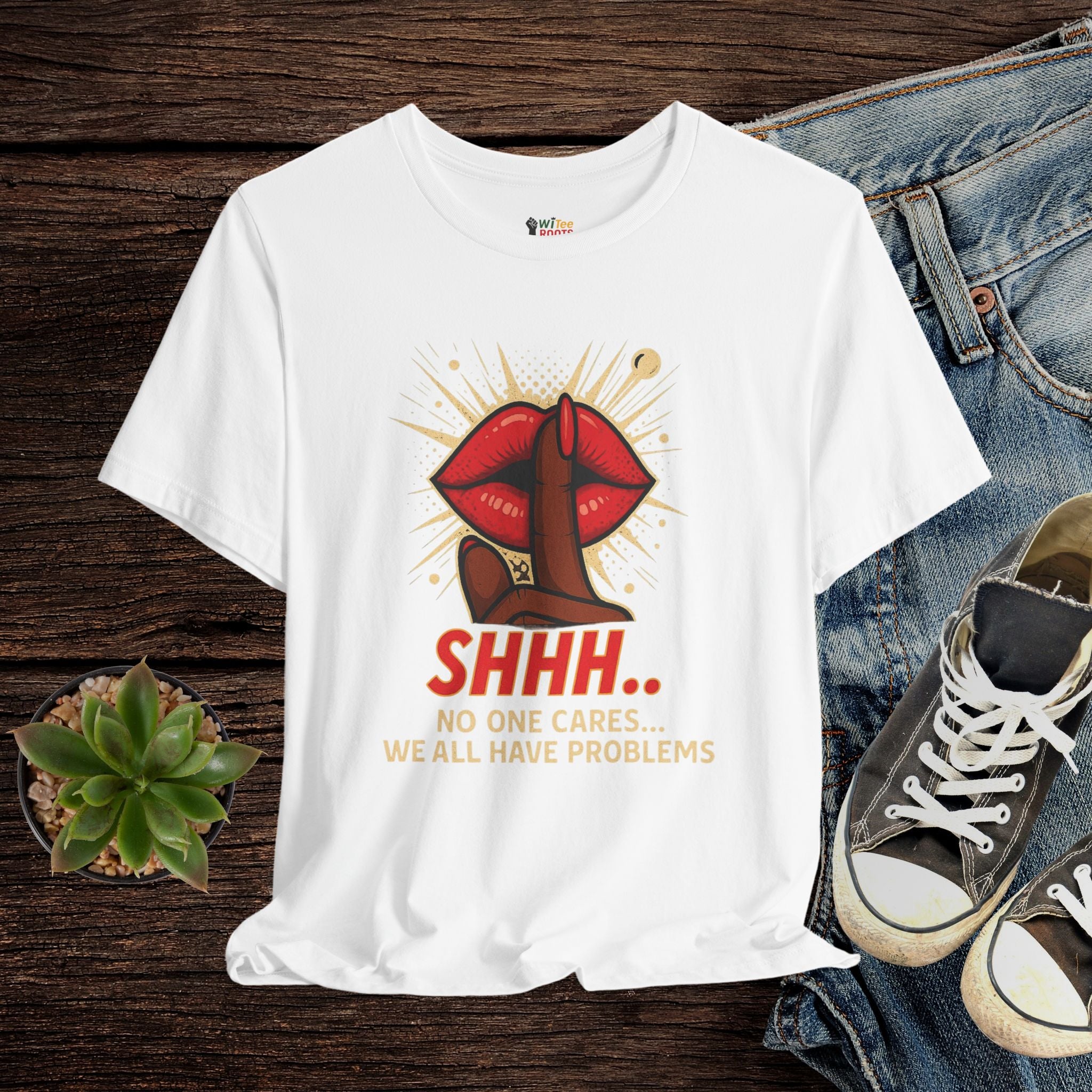 White t-shirt with graphic design and text on a wooden surface with jeans and sneakers.