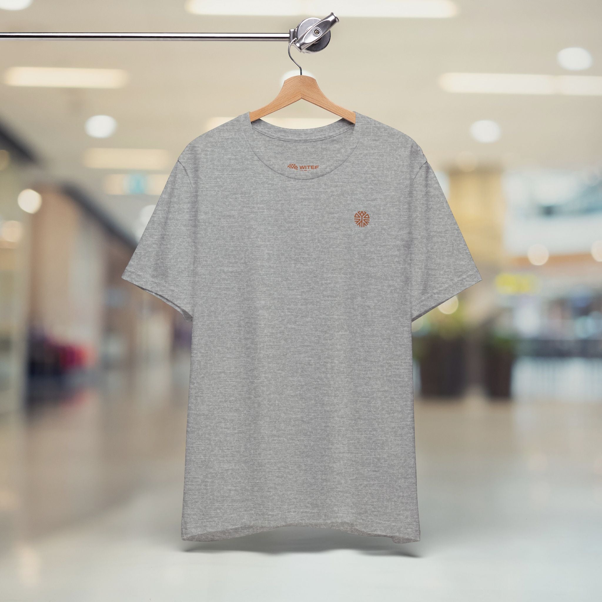 Gray t-shirt with a logo on a hanger against a blurred indoor background