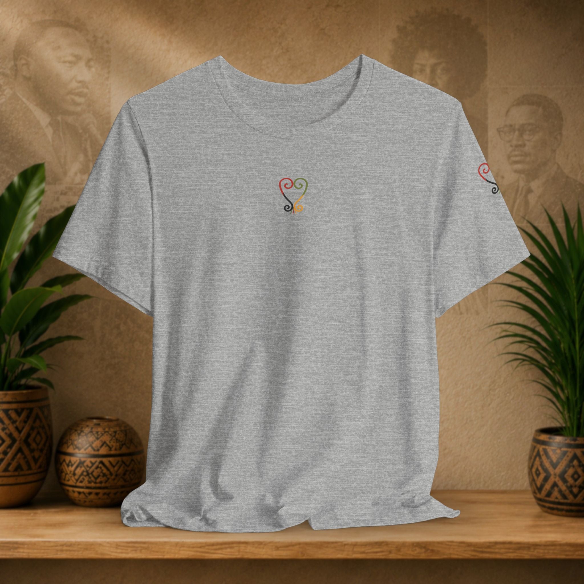 Gray t-shirt with a colorful design on a wooden surface with plants and a textured wall background