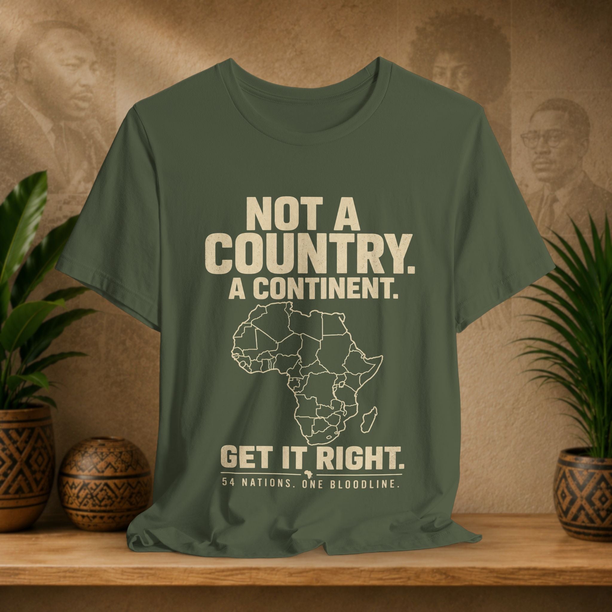 Green t-shirt with a map of Africa and text on a wooden surface with plants and a decorative item.