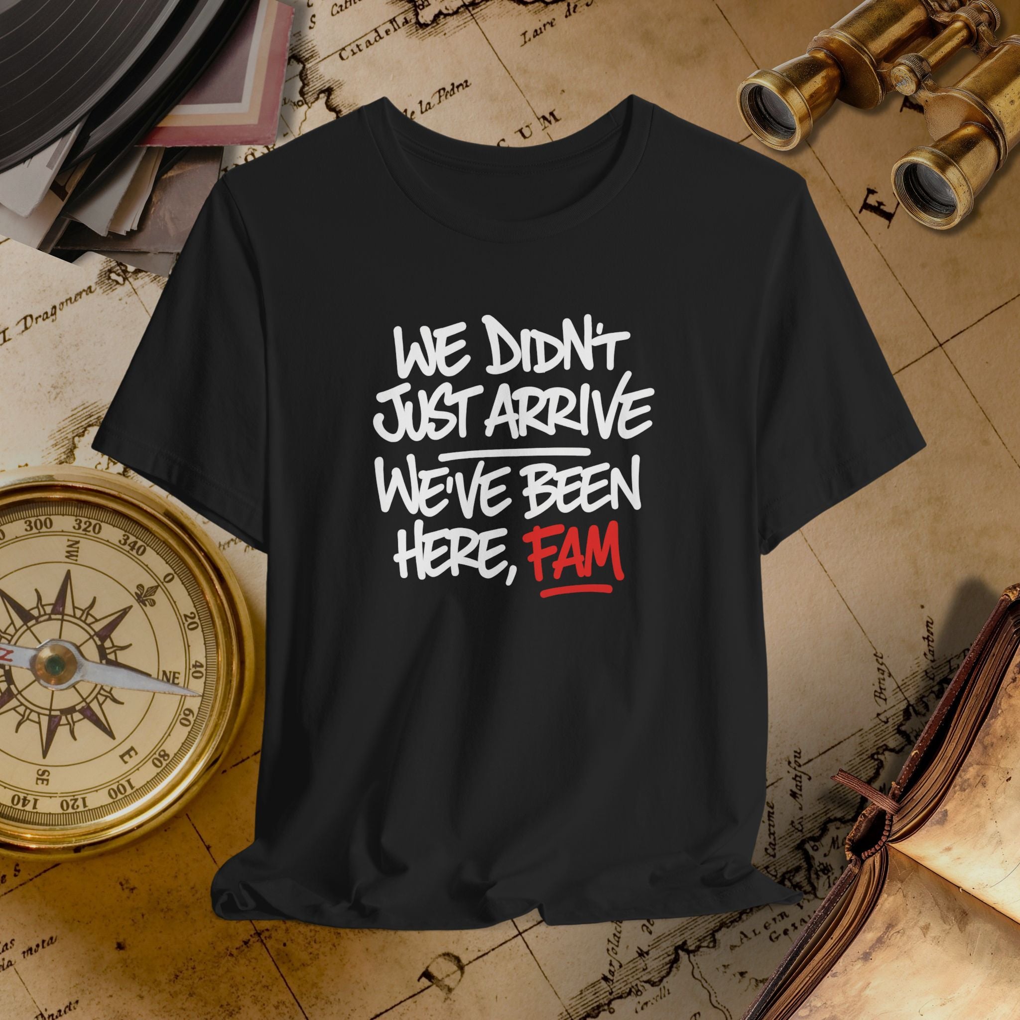 Black t-shirt with text 'WE DIDN'T JUST ARRIVE WE'VE BEEN HERE, FAM' on a vintage map background.
