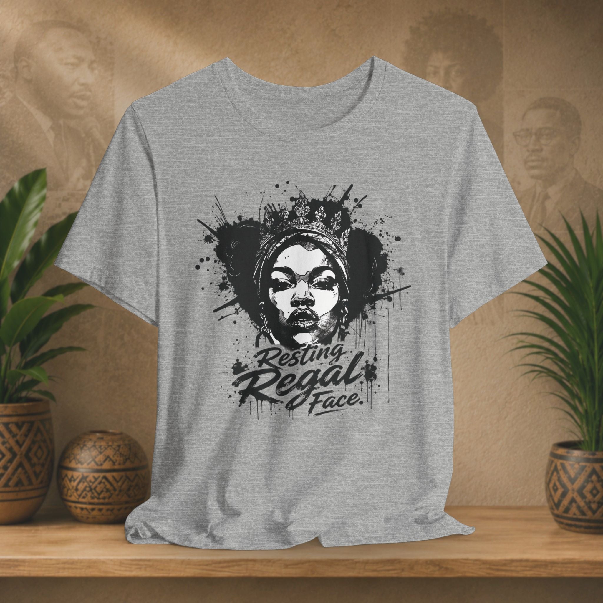 Gray t-shirt with a graphic design of a woman's face and text on a wooden surface with plants.