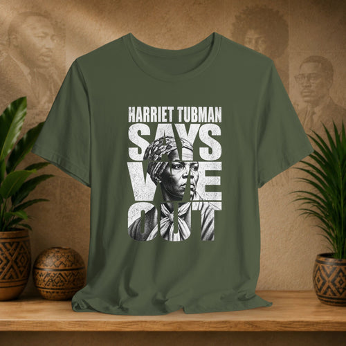 Green t-shirt with Harriet Tubman graphic and text on a wooden surface with plants and decorative items.
