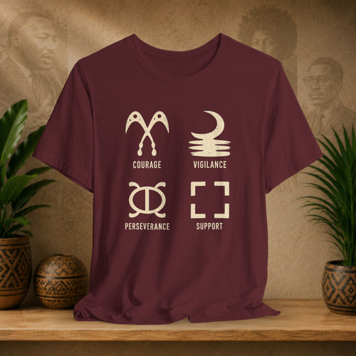 Maroon t-shirt with white symbols and text on a wooden surface with plants and a textured wall background