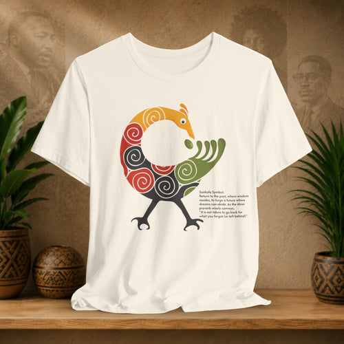 Beige t-shirt with a colourful bird design on a wooden surface with plants and a textured wall in the background