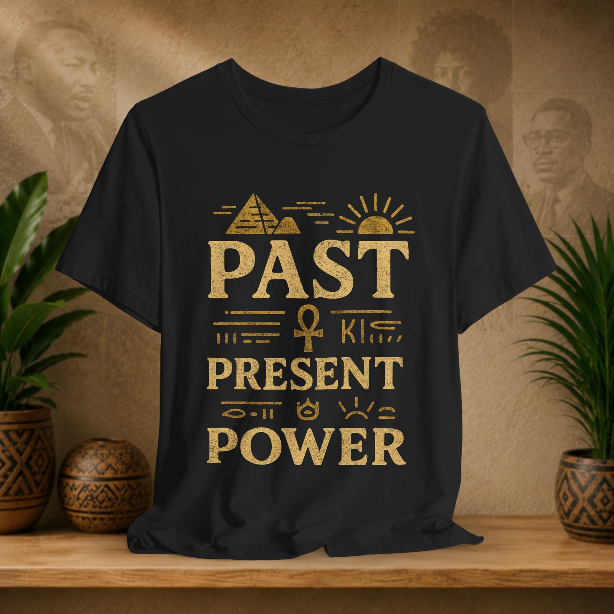 Black t-shirt with gold text and symbols on a wooden surface with plants and decorative items.