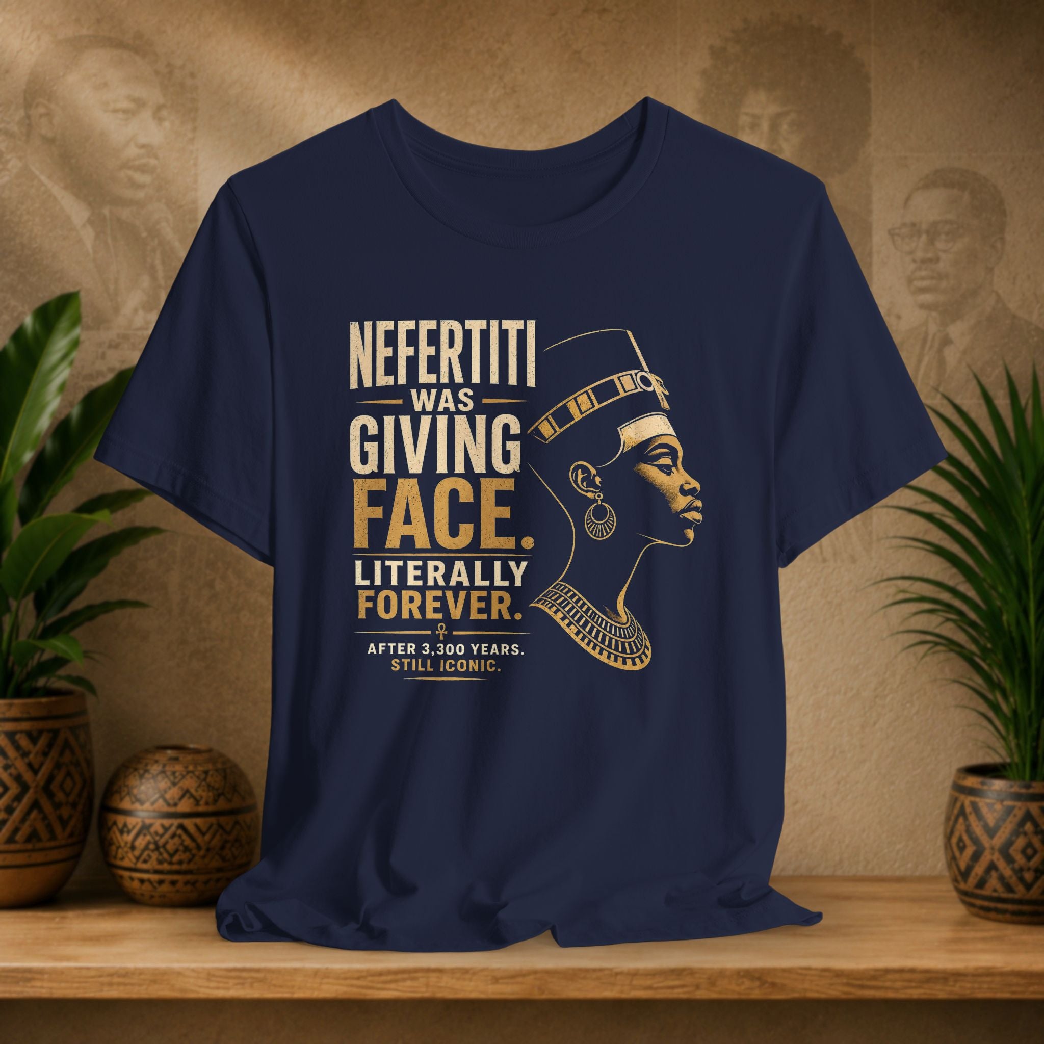 Navy blue t-shirt with graphic of Nefertiti and humorous text on a wooden surface with plants and decorative items.