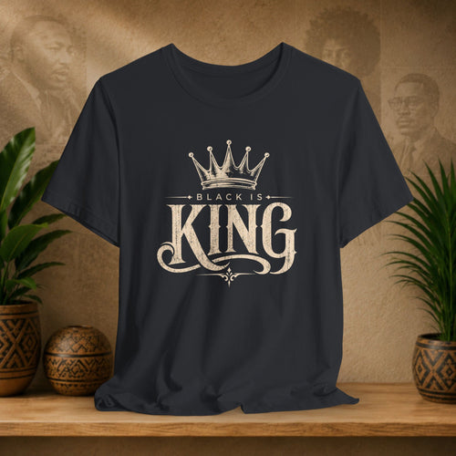 Black t-shirt with 'Black is King' design on a wooden surface with plants and decorative items in the background.