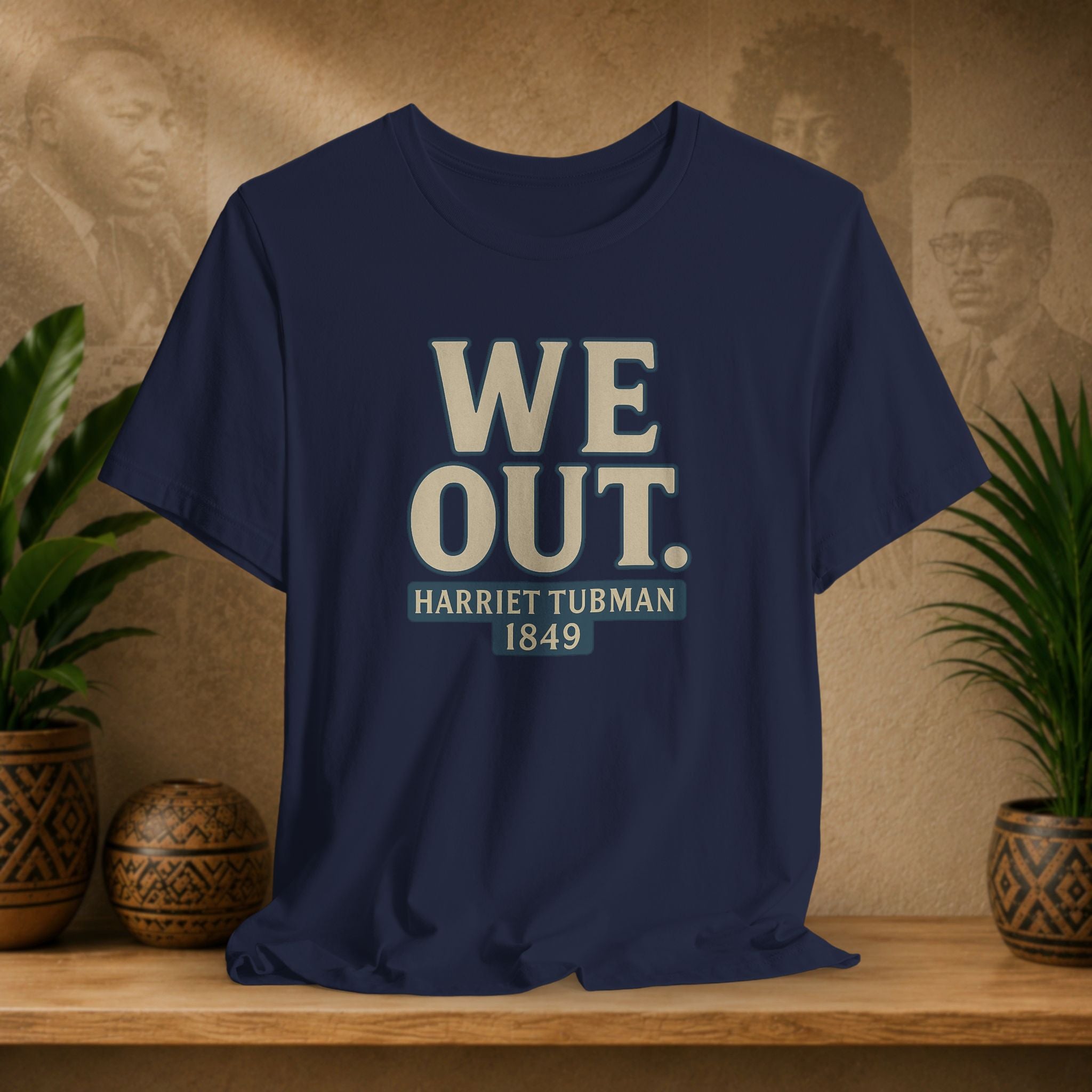 Navy blue t-shirt with 'WE OUT. HARRETT TUBMAN 1849' text on a wooden surface with decorative items.
