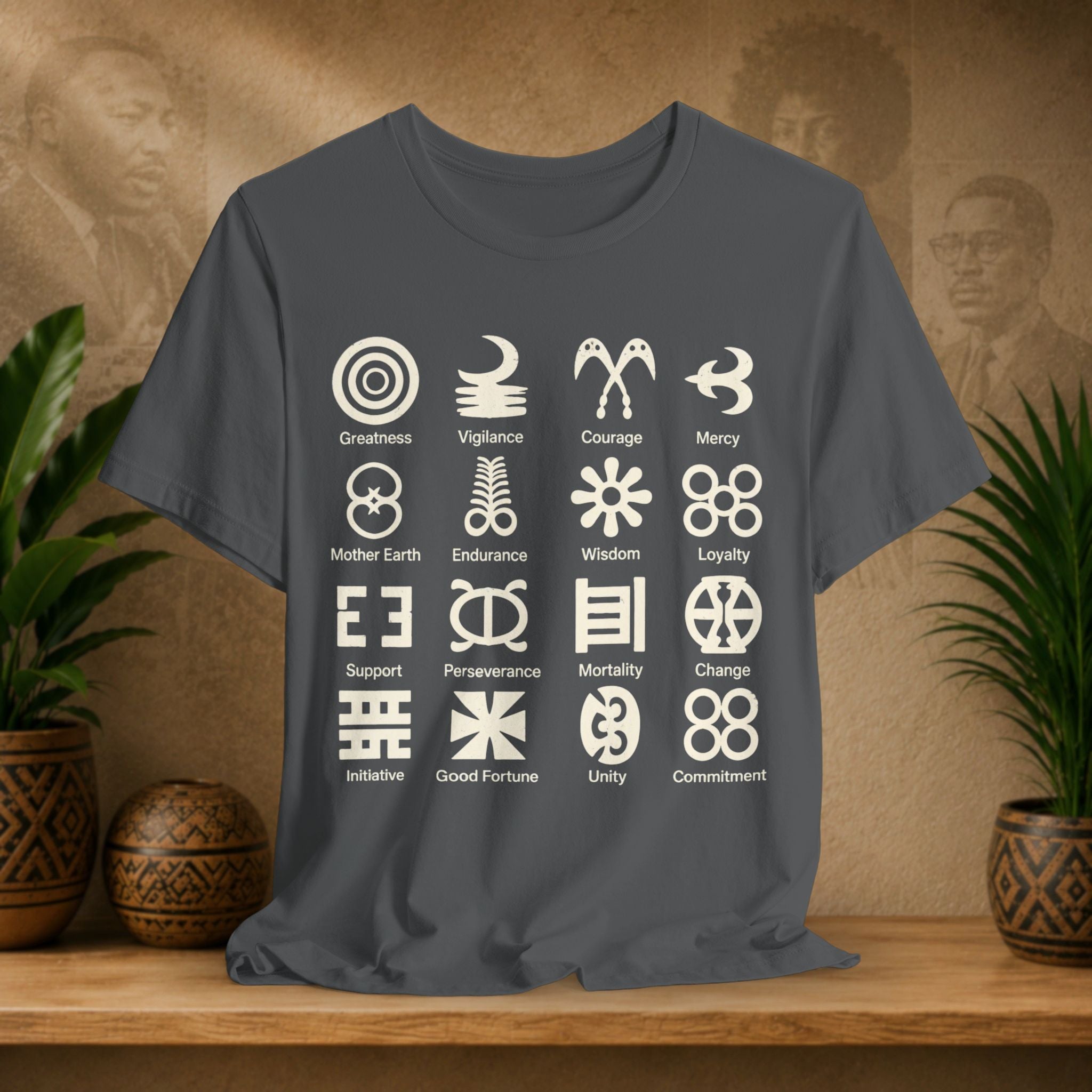 Gray t-shirt with white symbols and text on a wooden surface with plants and a textured wall background