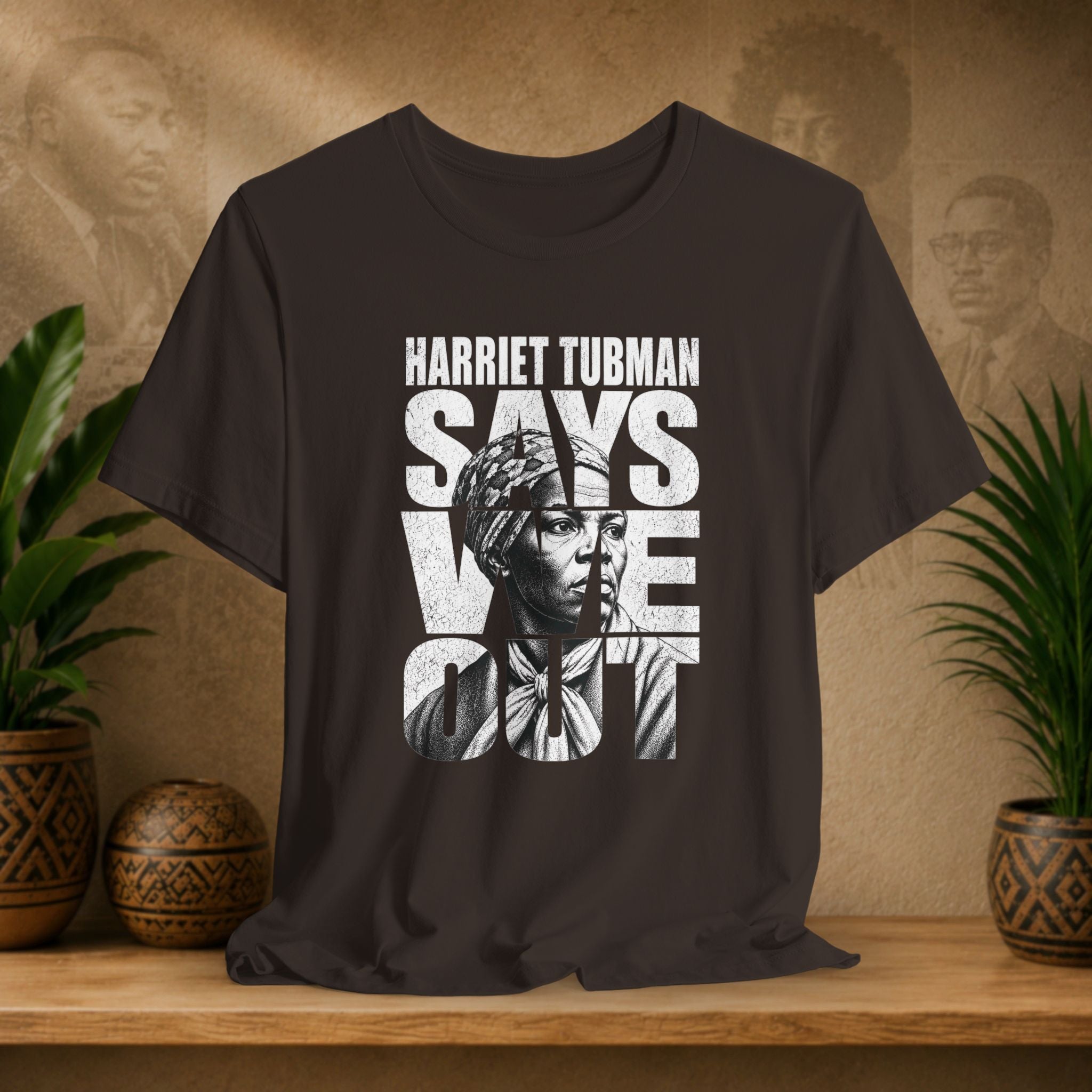Brown t-shirt with Harriet Tubman graphic and text on a wooden surface with plants and decorative items.