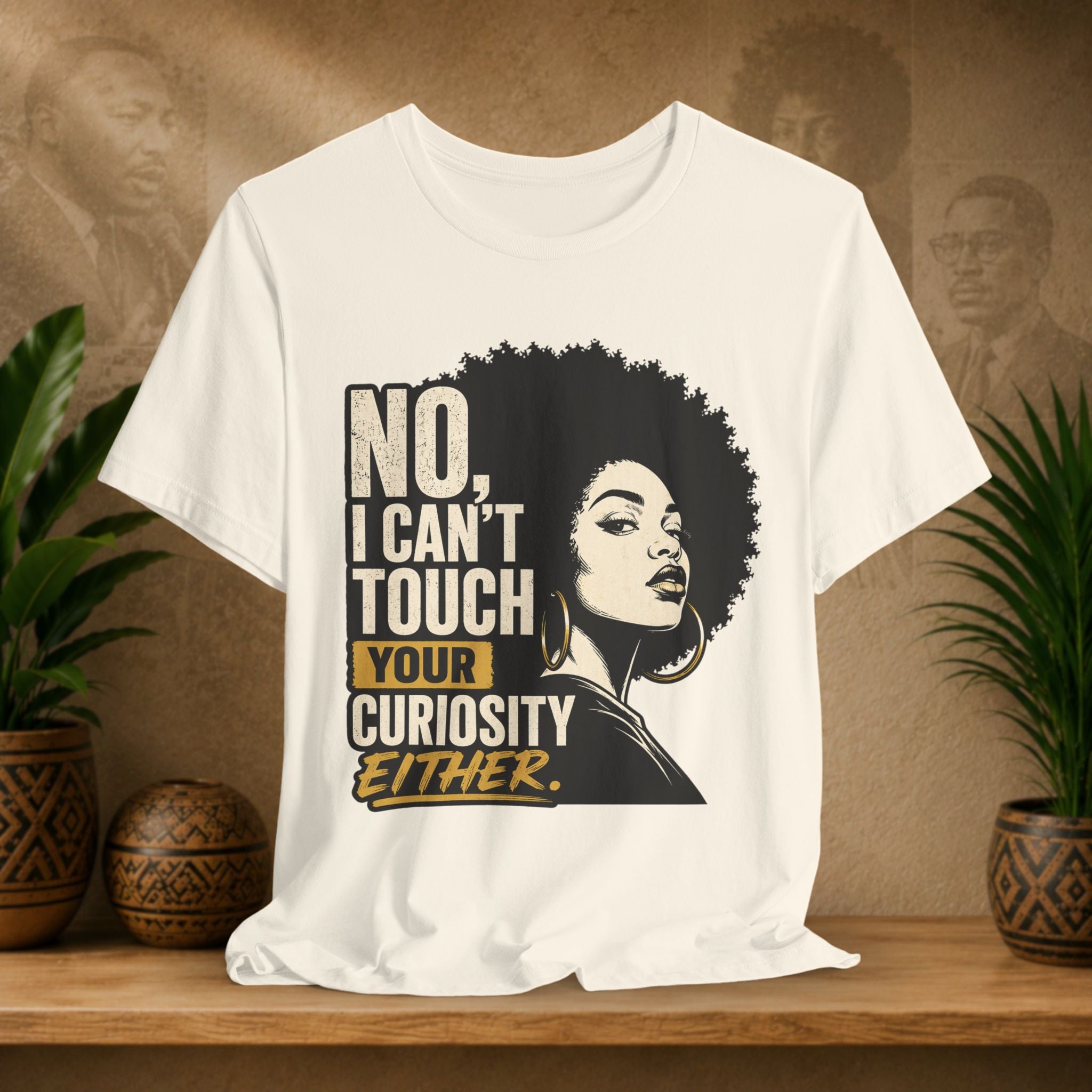Beige t-shirt with a graphic of a woman with an afro and text on a wooden surface with plants and a brown wall background.