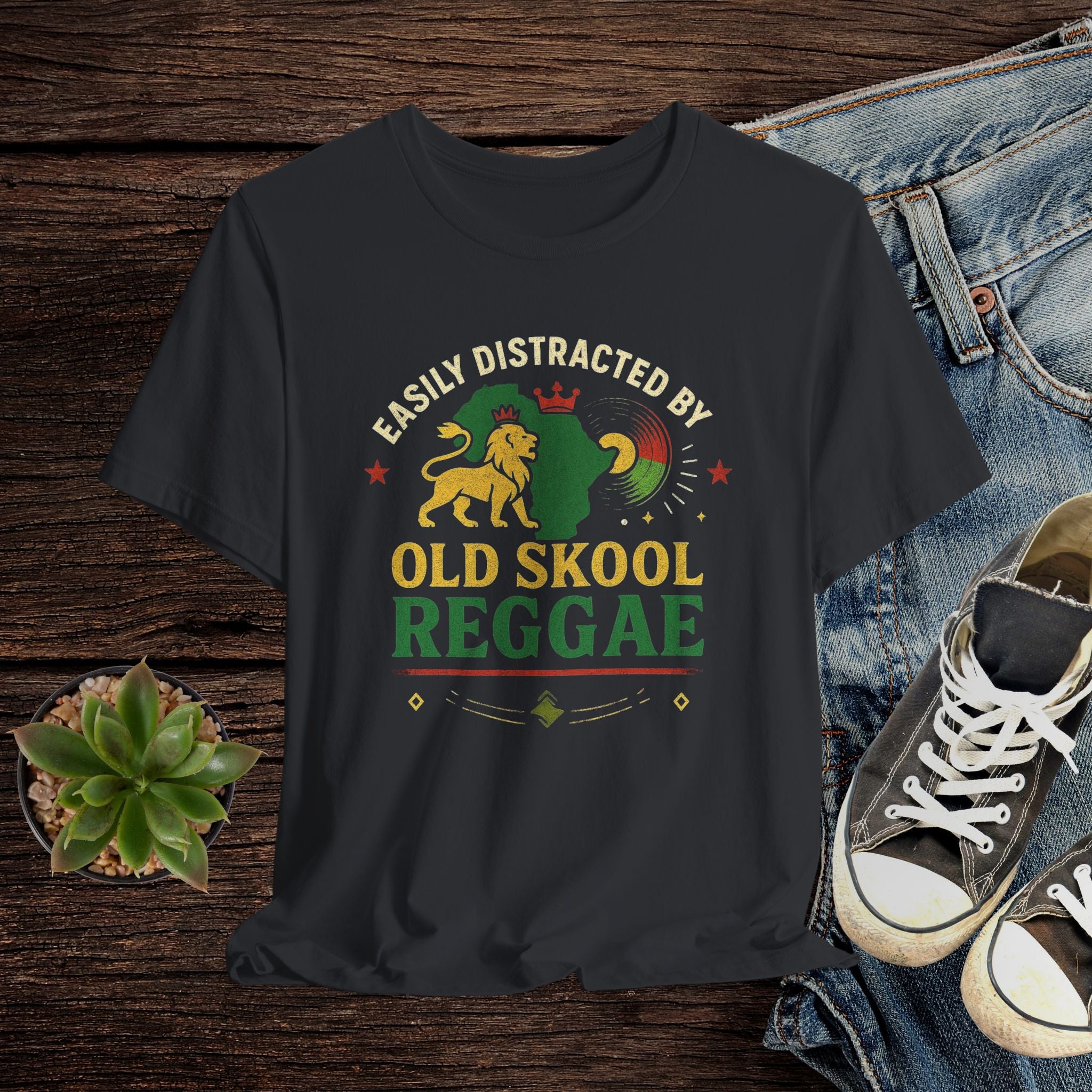Black t-shirt with 'Easily Distracted by Old Skool Reggae' design on a wooden surface with jeans and sneakers.