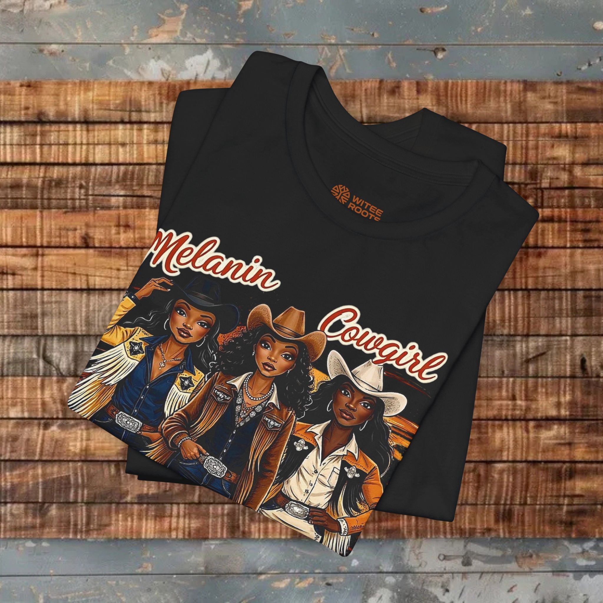 Black t-shirt with 'Melanin Cowgirl' design on a wooden surface
