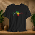 Black t-shirt with a colorful Africa map design on a wooden surface with plants and a textured wall in the background.