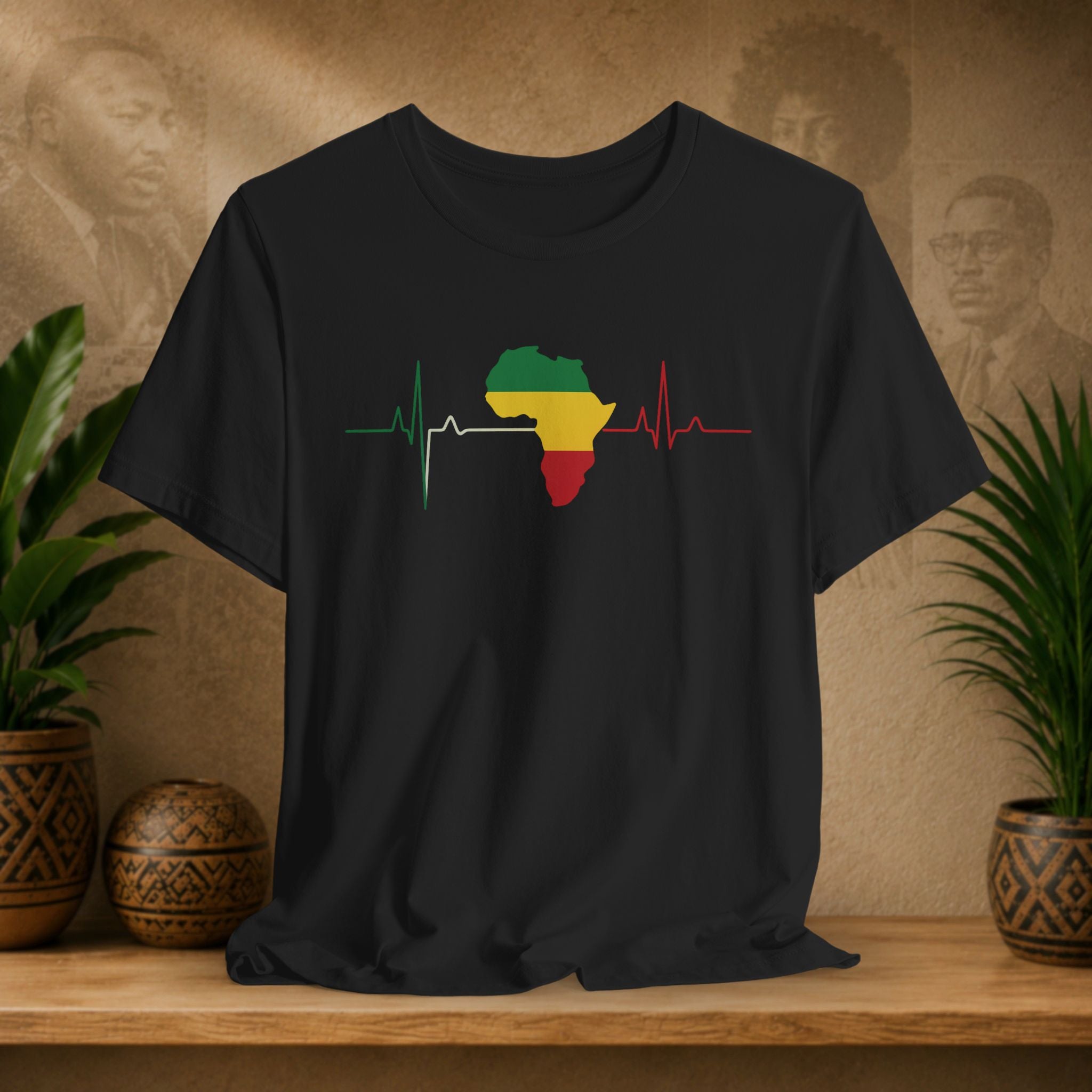 Black t-shirt with a colorful Africa map design on a wooden surface with plants and a textured wall in the background.