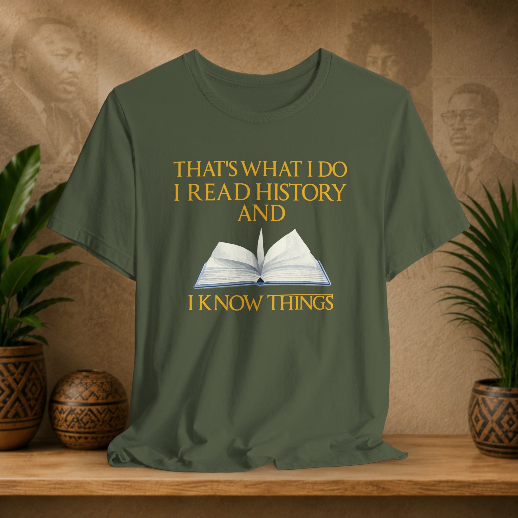 Green t-shirt with a book graphic and text on a wooden surface with plants and decorative items.