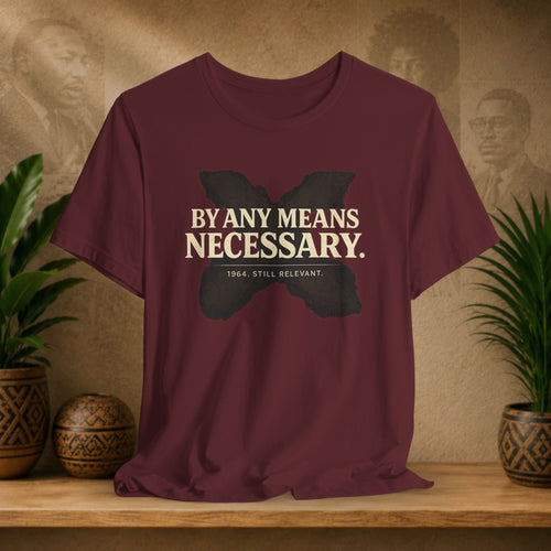Maroon t-shirt with a butterfly graphic and text on a wooden surface with plants and a textured wall in the background.