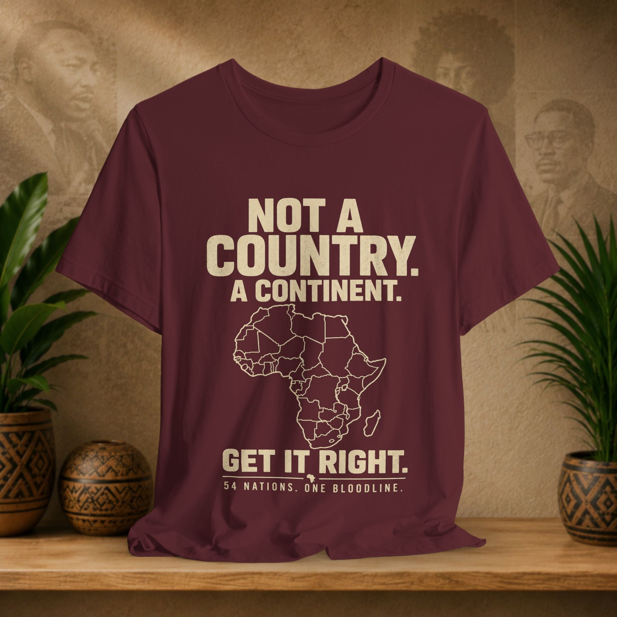 Maroon t-shirt with white text and Africa map on a wooden surface with plants and wall art in the background