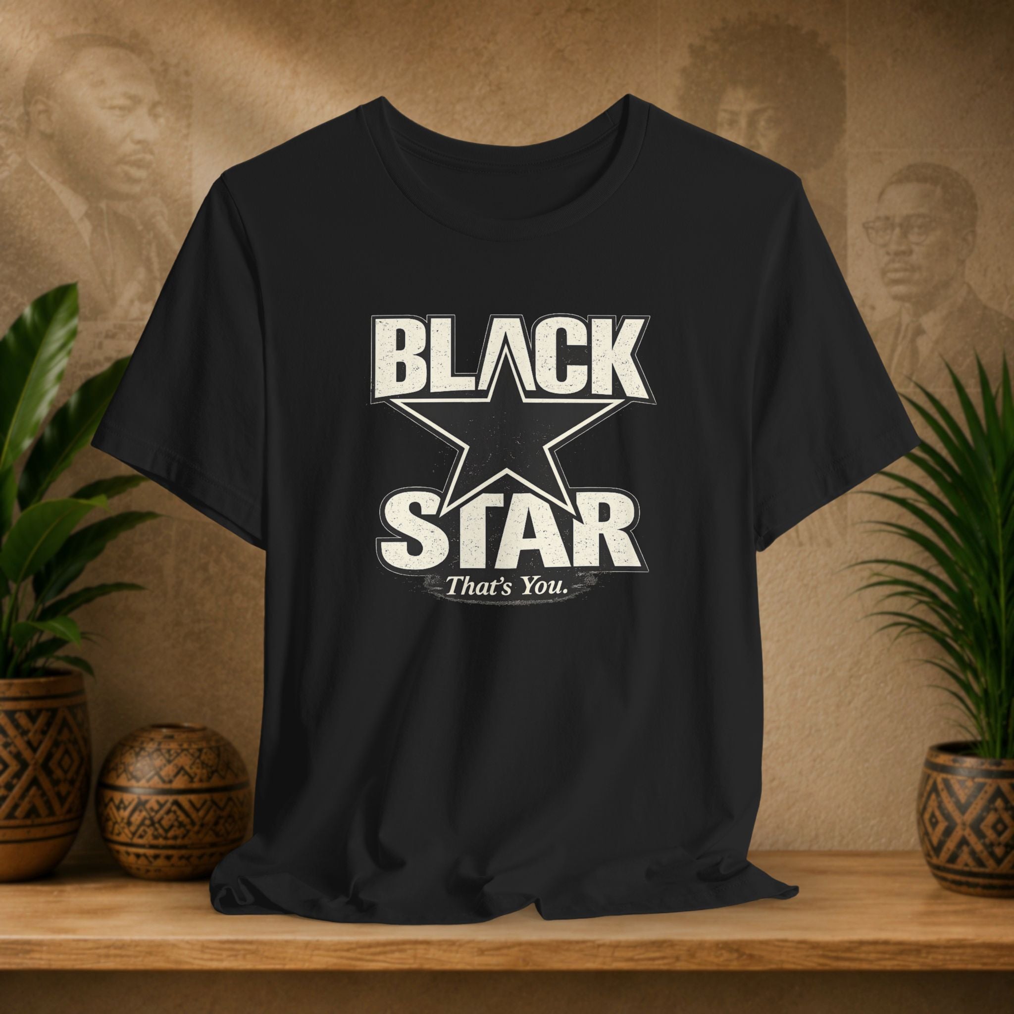 Black t-shirt with 'BLACK STAR That's You' design on a wooden surface with plants and a textured wall background.