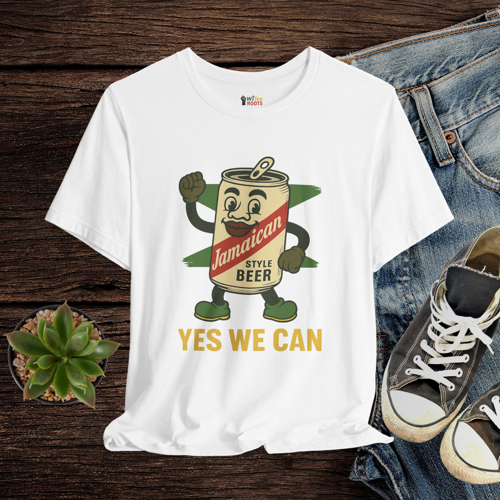 White t-shirt with a cartoon beer can design and 'Yes We Can' text, displayed with jeans and sneakers on a wooden surface.