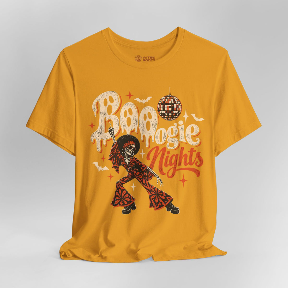 A mustard yellow graphic t-shirt featuring a Day of the Dead theme with a dancing skeleton, skulls, bats, and a disco ball, set against a light gray studio background.