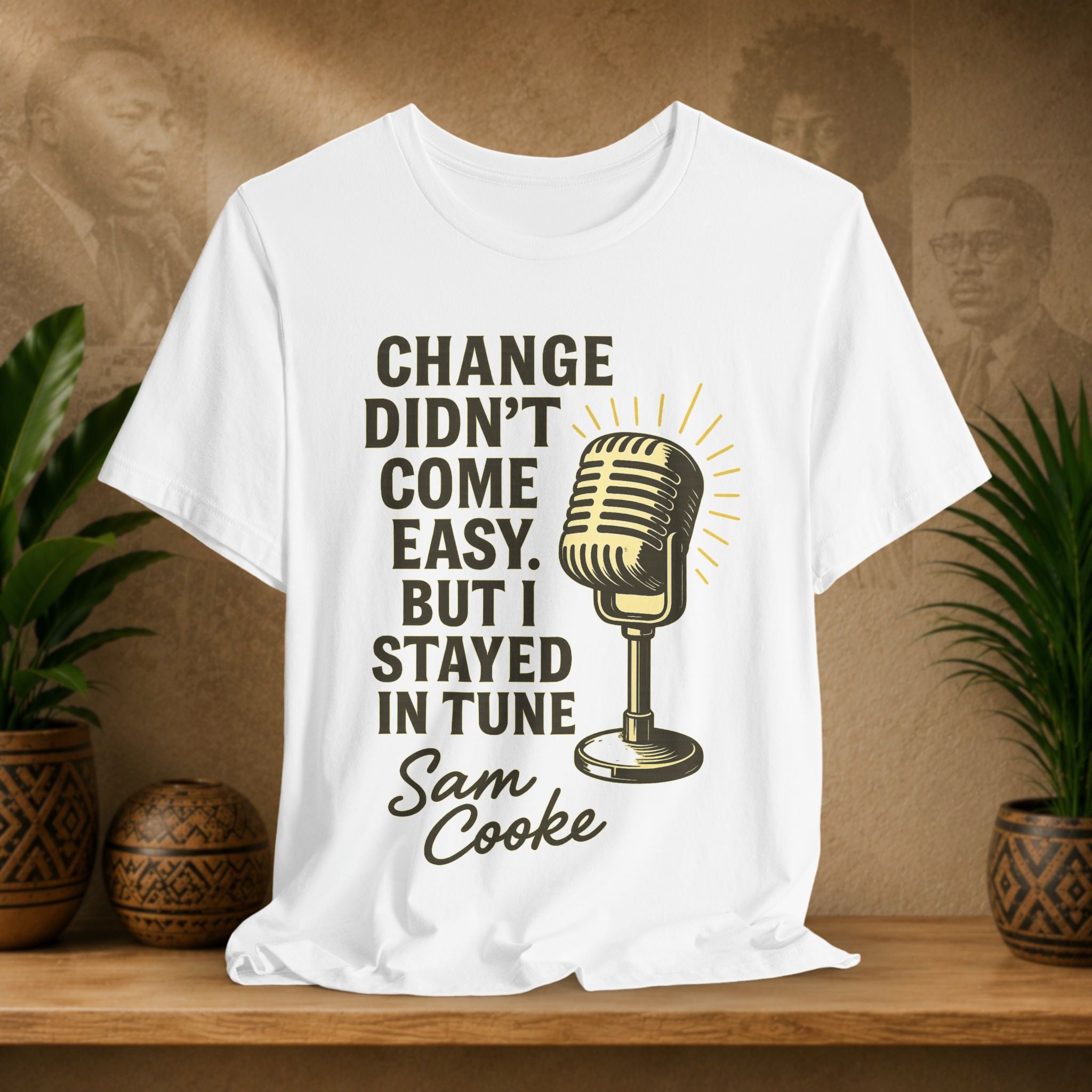 White t-shirt with microphone graphic and text on a wooden surface with plants and a brown background
