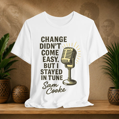 White t-shirt with microphone graphic and text on a wooden surface with plants and a brown background